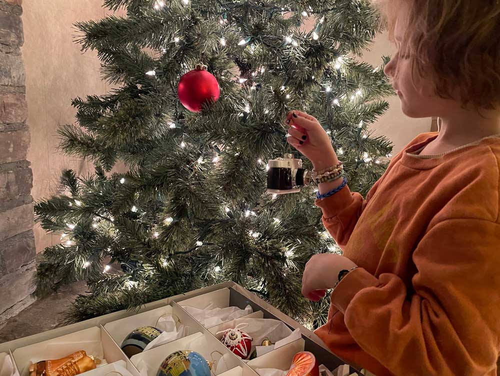 Young girl decorating Christmas tree with ornaments from an Archival Methods dray storage box with divided compartments filled with glass ornaments. 